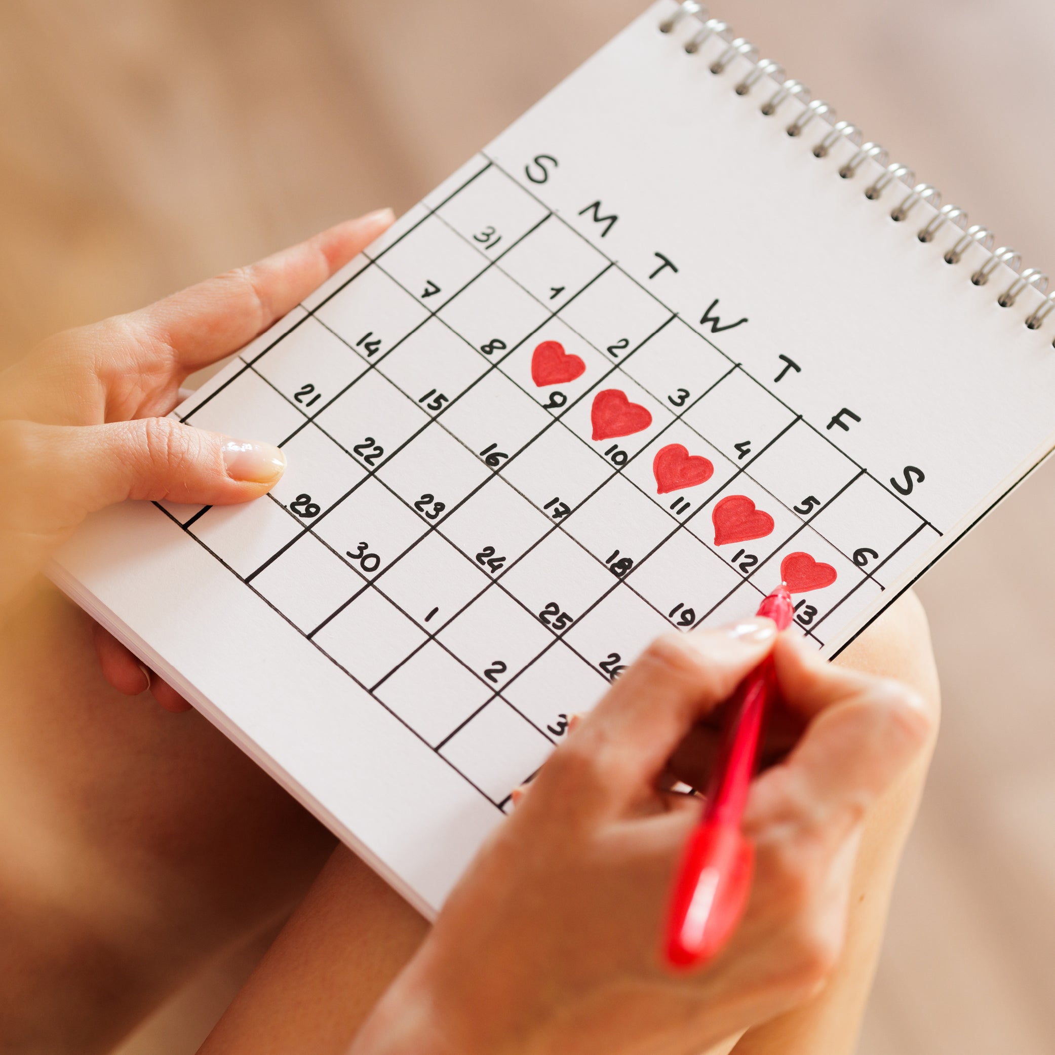 Women marketing calendar with love hearts marking when her period arrived