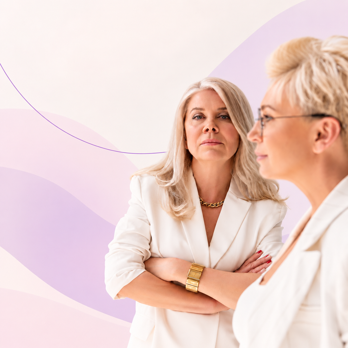  Two midlife women in white blazers, one looking directly at the camera, against a soft cream and lavender 